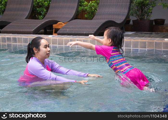 Happy Asian family enjoying summer vacation in swimming pool at resort.