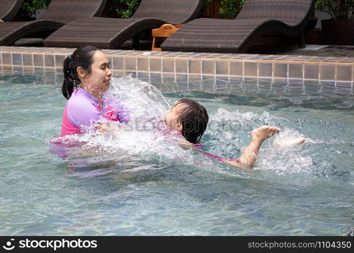 Happy Asian family enjoying summer vacation in swimming pool at resort.