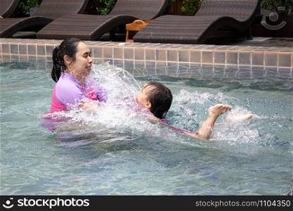 Happy Asian family enjoying summer vacation in swimming pool at resort.