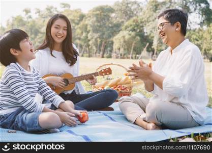Happy Asian family having fun and enjoying while playing ukulele in the park. The concept of lifestyle in family holiday