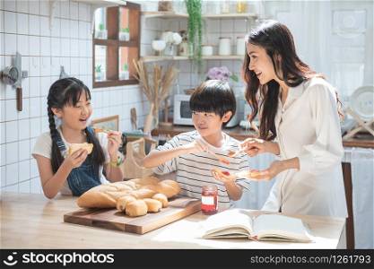 Happy asian family in the kitchen. mother and son and daughter spread strawberry yam on bread, leisure activities at home.