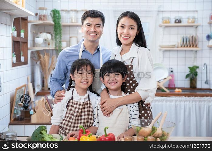 Happy asian father,mother,child standing and smile in kitchen.Healthy parent prepare salad.