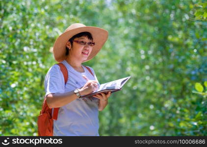 Happy Asian female tourist smiling while taking notes on nature pathway in mangrove forest at natural parkland, ecotourism concept