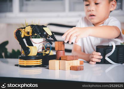 Happy Asian little boy using remote control playing robotic machine arm for pick up wood block, Funny learning successful getting a lesson control robot arm, Technology science education concept