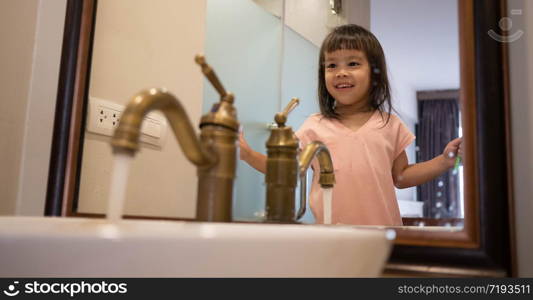 Happy Asian little child girl brushing teeth in the bathroom in morning. Oral hygiene concept.