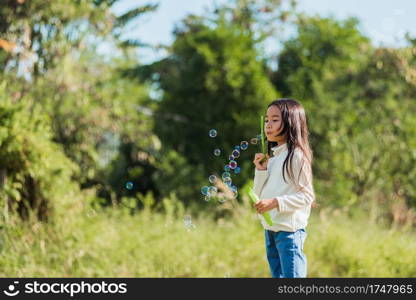 Happy Asian little cute girl child having fun and enjoying outdoor play blowing soap bubbles during in the garden park on a sunny day, summer time