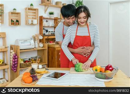 Happy Asian Lover or couple hugging and cooking in happiness action in the kitchen room at the modern house, Couple and life style concept.