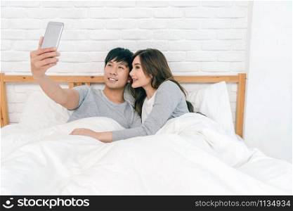 Happy Asian Lover using the technology smart phone for selfie on the bed in bedroom at home, Couple selfie concept,