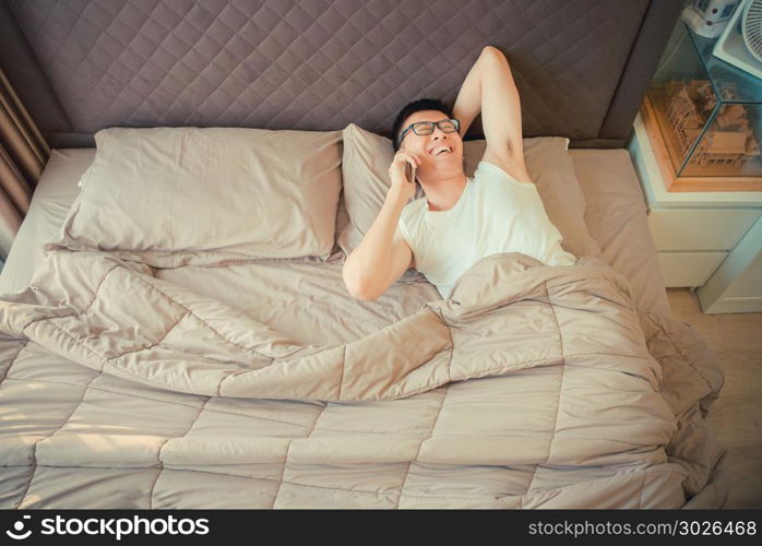 Happy Asian man talking on the phone on bed