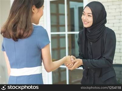 Happy asian muslim businesswoman sales manager shake hand of asian lady client make deal with female customer at meeting with laptop, diverse women partnership, respect and collaboration concept