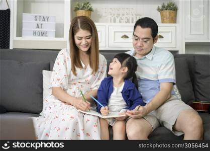 Happy asian parent teaching little cute daughter to do homework and drawing picture together at home.