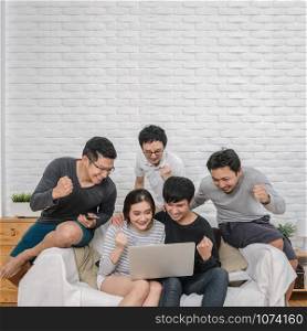 Happy Asian people group sitting and using the digital laptop in cheerful and celebration action over the sofa of living room at modern home, Couple successfull and lifestyle concept