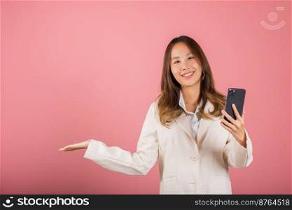 Happy Asian portrait beautiful cute young woman excited holding mobile phone blank screen presenting product with palm of hand at empty, studio shot isolated on pink background, female look camera