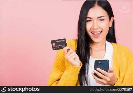 Happy Asian portrait beautiful cute young woman excited smiling hold mobile phone and plastic debit credit bank card, studio shot isolated on pink background, female using smartphone online shopping