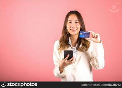 Happy Asian portrait beautiful cute young woman excited smiling hold mobile phone and plastic debit credit bank card, studio shot isolated on pink background, female using smartphone online shopping