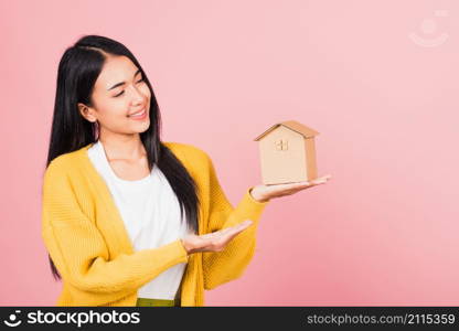 Happy Asian portrait beautiful cute young woman excited smiling holding house model on hand, studio shot isolated on pink background, broker female hold home real estate insurance and banking concept