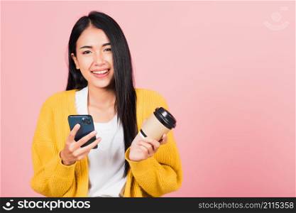 Happy Asian portrait beautiful cute young woman excited smiling holding mobile phone and coffee to go, studio shot isolated on pink background, female using smartphone with coffee cup take away