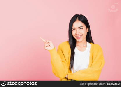 Happy Asian portrait beautiful cute young woman standing smiling indicate finger empty space looking to camera, studio shot isolated on pink background, Thai female pointing index out with copy space