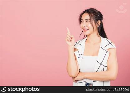 Happy Asian portrait beautiful cute young woman standing smiling indicate finger empty space looking to space, studio shot isolated on pink background, Thai female pointing index out with copy space