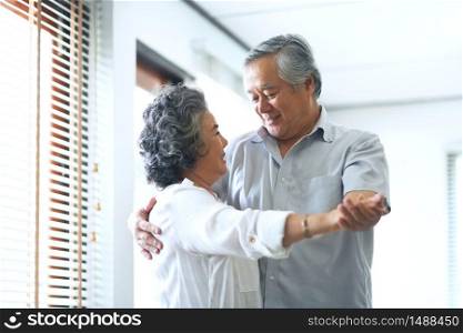 Happy Asian Senior couple dancing and smiling at home. Celebrating Wedding Anniversary.