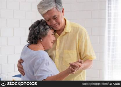 Happy Asian senior couple enjoy slow dancing at living room in house with warm love emotion.grandmother snuggle grandfather