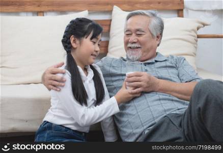 Happy asian senior elderly grandfather have grandchild look after and take care with giving milk and kiss on cheek while sitting on sofa at home,retirement health lifestyle concept.