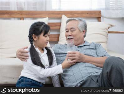 Happy asian senior elderly grandfather have grandchild look after and take care with giving milk and kiss on cheek while sitting on sofa at home,retirement health lifestyle concept.
