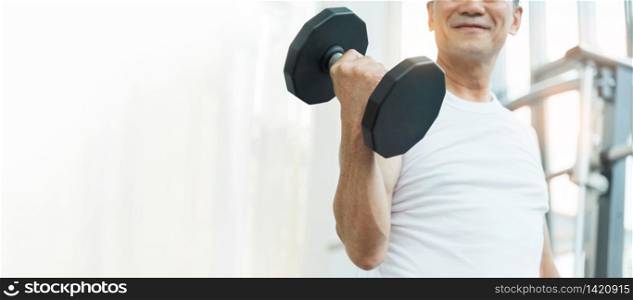 Happy Asian Senior Fitness man lifting dumbbell while exercise at the gym. Strong Sporty Elderly male in white sportswear smiling while workout. Lifestyle, Healthy. Banner, Web.