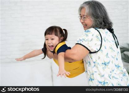 Happy Asian senior grandmother holding and playing with granddaughter in the living room, happy grandma wearing glasses and granddaughter embracing show love and care, Love and protection concept