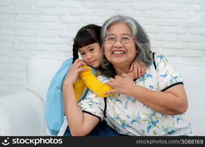 Happy Asian senior grandmother sit on a couch and granddaughter