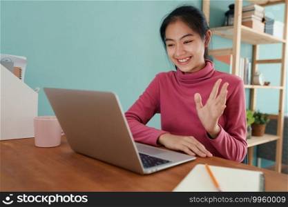 Happy Asian student waving in greeting online tutor on a laptop computer at home. Asia woman Wear long sleeves pink, Concept of online learning at home