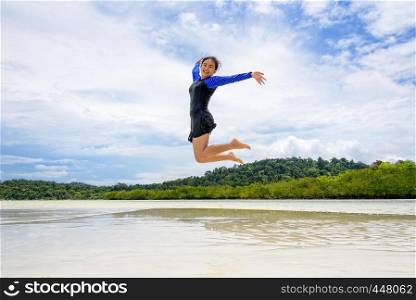 Happy asian teen girl wearing a swimsuit jumping fun on the beach of Ko Ra Wi under the blue sky during the sea tour on vacation summer holiday at Ko Lipe island in Tarutao National Park, Satun, Thailand. Happy asian teen girl jumping fun on the beach