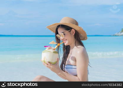 Happy Asian woman, a sexy Thai lady, drinking coconut water at turquoise sea near Phuket beach during travel holidays vacation trip outdoors at natural ocean or island at noon, Thailand.