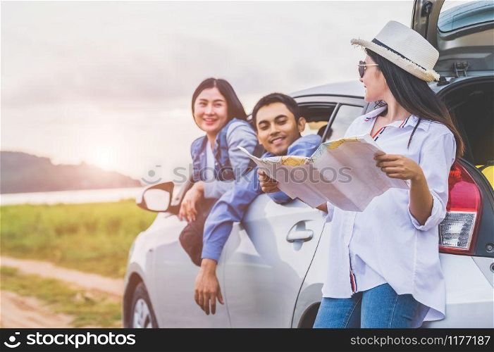 Happy Asian woman and her friends standing by car on coastal road at sunset. Young girl having fun during road trip. People lifestyles and travel vacation concept. Friendship journey and Outdoor tour