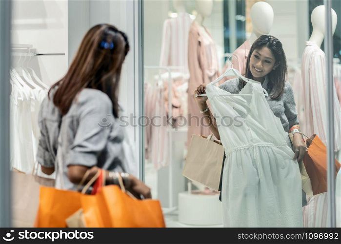 Happy Asian woman choosing clothes with reflection of glass in shop store shop with happy action at department center