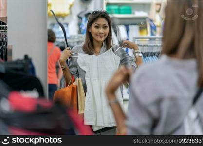 Happy Asian woman choosing clothes with reflection of glass in store shop with happy action at department center