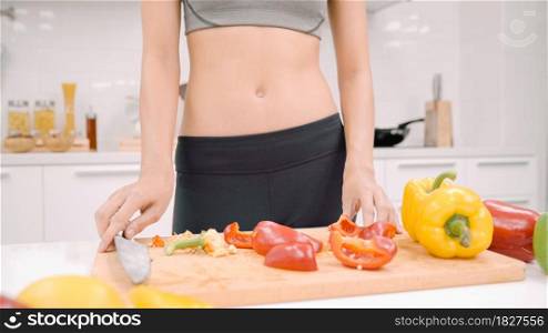 Happy Asian woman cut lots of bell pepper prepare ingredient for making food in the kitchen, female use organic vegetable for healthy food at home. Lifestyle women making health food concept.