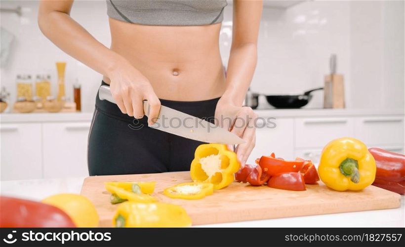 Happy Asian woman cut lots of bell pepper prepare ingredient for making food in the kitchen, female use organic vegetable for healthy food at home. Lifestyle women making health food concept.