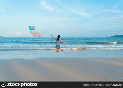Happy Asian woman holding colorful balloons at the beach during travel trip on holidays vacation outdoors at ocean or nature sea at noon, Phuket, Thailand