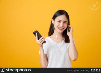 Happy Asian woman holding smartphone and listening to music on pink background.