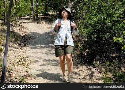 Happy Asian woman in a hat with a backpack trekking enjoying nature in the tropical forest. Travel and Lifestyle Concepts