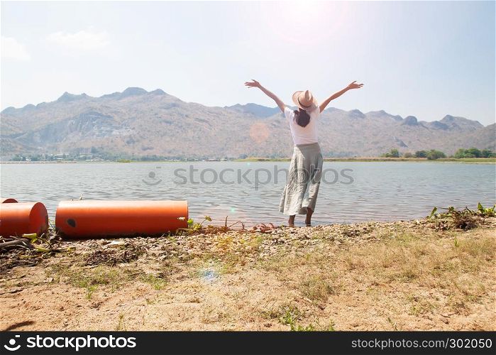 Happy asian woman in casual style clothing raised up arms and standing in the river with mountain view on background