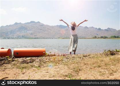 Happy asian woman in casual style clothing raised up arms and standing in the river with mountain view on background
