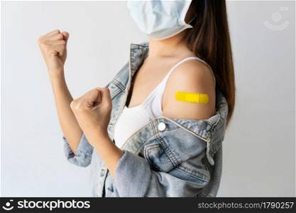Happy Asian woman in medical face mask showing arm with adhesive plaster after Covid-19 vaccine injection on white background. Antiviral Immunization concept. Copy space.