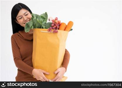 Happy Asian woman is smiling and carries a shopping paper bag after the courier from the grocery came to deliver his goods at home. Concept of Supermarket delivery for a new lifestyle