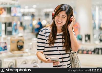 Happy Asian woman listening and testing technology Earphone or headphones in store shop or department store