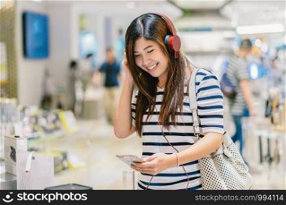 Happy Asian woman listening and testing technology Earphone or headphones in store shop or department store
