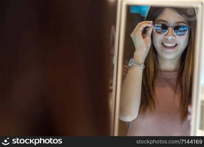 Happy Asian woman looking and choosing eyeglasses in store shop at department store, shopping and fashion concept