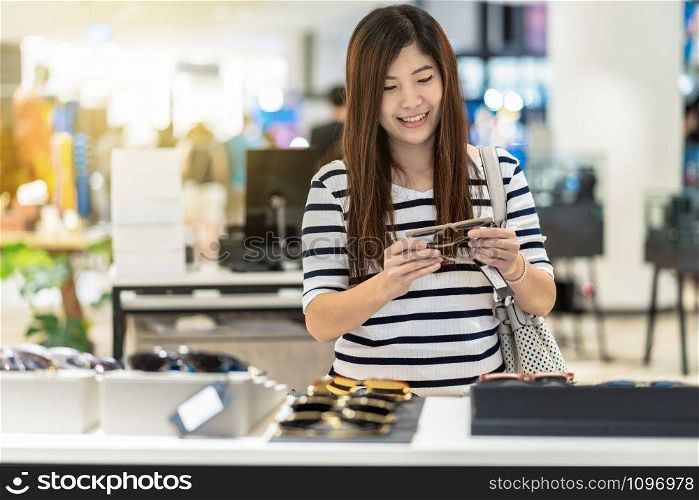 Happy Asian woman looking and trying the glasses in store shop at department store, shopping and fashion concept
