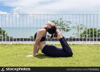Happy Asian woman practice yoga king cobra or Raja Bhudjangasana pose to stretching her muscle with beautiful sea in background,Feeling so comfortable and relax in holiday,Healthy Concept